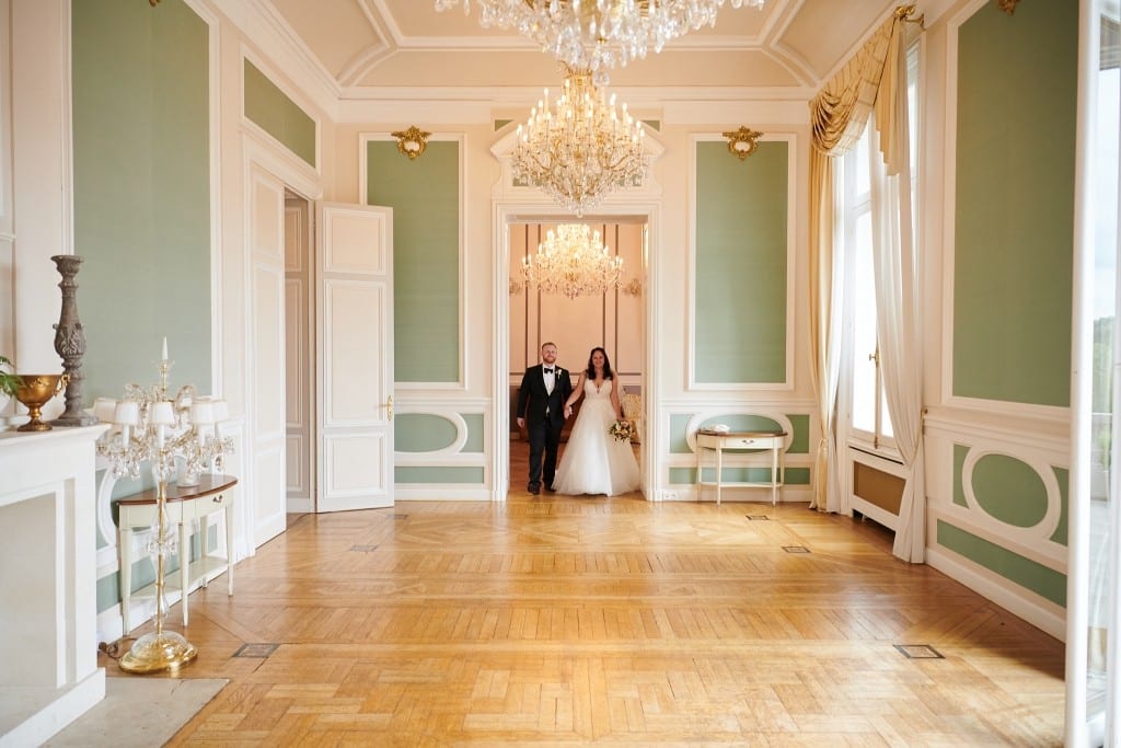 Couple de mariés avançant dans un salon haussmannien aux murs vert d'eau pour un mariage à Paris