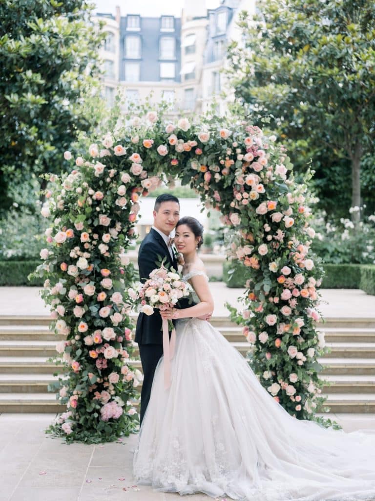 Mariés posés sous une arche florale rose et pêche lors d'un mariage printanier à Paris