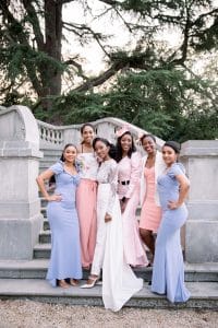 Mariée entourée de ses demoiselles d'honneur en robes pêche et bleu pastel sur un escalier de jardin