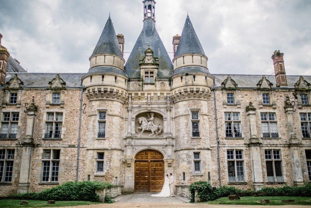 Couple de mariés s'embrassant devant le portail majestueux d'un château français à tourelles